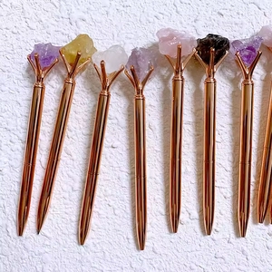 Close-up of rose gold pens featuring various natural raw crystal stones on top