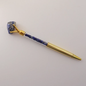 Detail of golden ballpoint pen featuring raw blue crystal top and stone chip filling