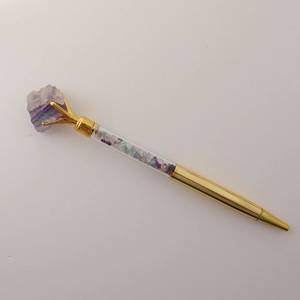 Macro detail of golden ballpoint pen featuring natural purple crystal and mixed gemstones