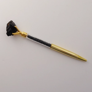 Detail of golden ballpoint pen featuring clear barrel filled with black crystal gravel
