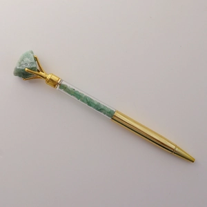 Detail of gold crystal ballpoint pen featuring a green raw gemstone top and crushed stones