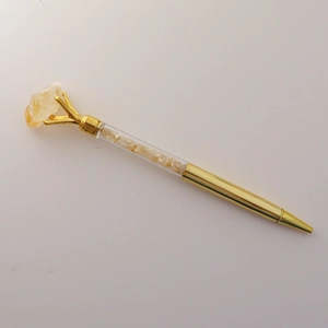 Detail of gold metal ballpoint pen with yellow crystal gravel and a raw stone top