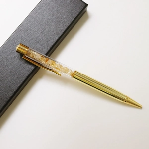 Close-up of golden metal pen filled with yellow crystals in a black gift box