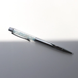 Macro detail of silver metal ballpoint pen with sky blue crystal gravel in transparent tube