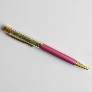 Macro view of crystal ballpoint pen with olive green stones and purple metal barrel