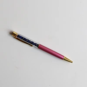 Detail of rose red metal ballpoint pen featuring a transparent chamber with blue crystals