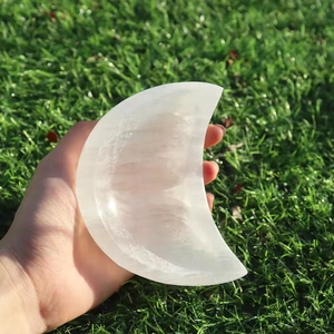 Close-up of hand holding a crescent moon selenite crystal bowl on green grass