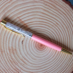 Close-up of pink crystal ballpoint pen with gold accents on a rustic wooden surface