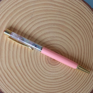 Macro view of crystal fragments inside a pink and gold metallic ballpoint pen on wood