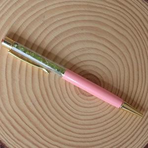 Close-up of pink crystal ballpoint pen with green stones on natural wood slice base