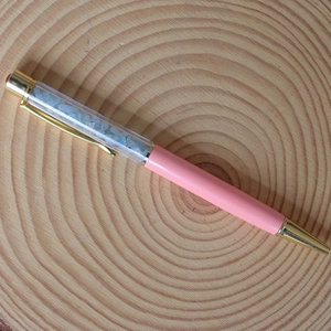 Detail of pink crystal ballpoint pen with sky blue crushed stones on a wooden tray
