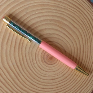 Macro detail of a pink ballpoint pen with green crystal stone fill on wood background