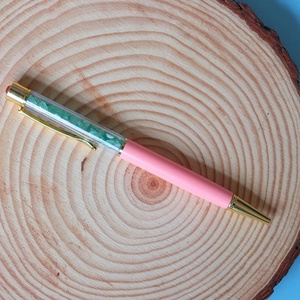 Close-up of elegant pink ballpoint pen filled with green crystal crushed stones
