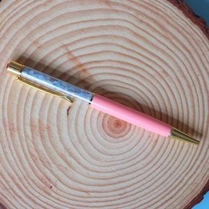 Close-up of a pink crystal ballpoint pen with blue crushed stones on a wooden slice