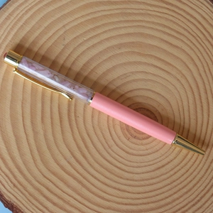 Macro detail of a pink crystal ballpoint pen with gold metal accents on a wooden stand