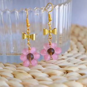 Détail de boucles d'oreilles en œil de chat rose avec nœud doré et crochets en argent S925
