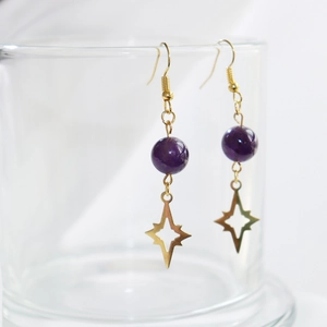 Detailed shot of amethyst gold earrings with star pendants hanging on a glass rim