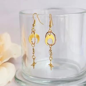 Close-up of golden moon and star earrings hanging on a glass rim with crystal detail