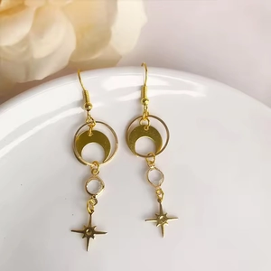 Detail of bohemian gold star and moon drop earrings hanging on a white ceramic plate