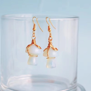 Detail of handmade wire-wrapped mushroom earrings with opal-like stones and gold hooks