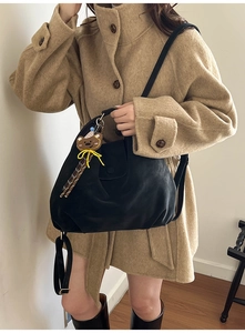 Close-up of black pleated leather tote bag with a brown bear pendant on a model