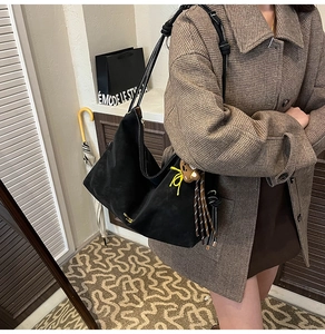 Nahaufnahme einer schwarzen Hobo-Tasche mit geknotetem Gurt und Quasten-Anhänger