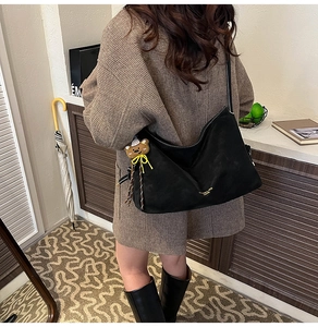 Detail der schwarzen Wildleder-Hobotasche mit weißen Nähten und Bärenanhänger-Accessoire