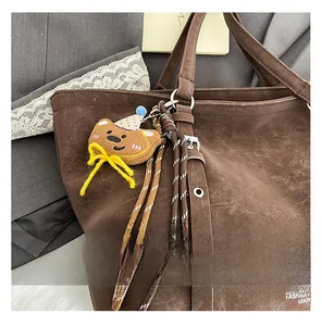 Detail of a brown knitted bear charm with a yellow bow attached to a vintage tote bag
