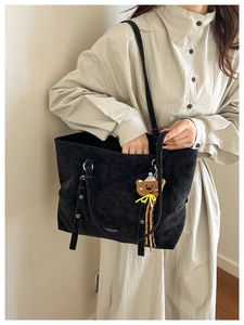 Detail of black suede tote bag with cute bear charm and fashion leather branding