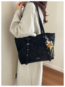 Detail of black vintage tote bag with buckle straps, matte texture, and plush doll charm