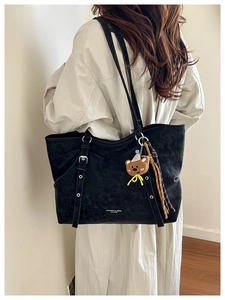 Detail of a large black tote bag with strap buckles and a cute bear charm on a model