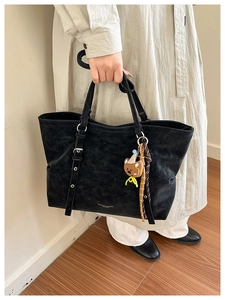 Detail of vintage black leather tote bag with logo print and cute brown bear charm