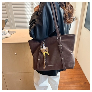Detail of deep brown matte leather tote bag with bear charm and fashion lettering