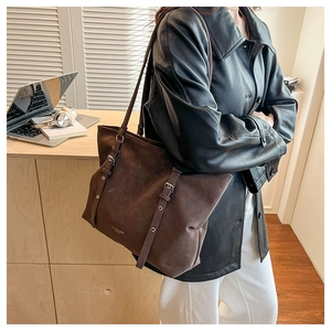Close-up of brown suede tote bag featuring silver buckles and decorative eyelet straps