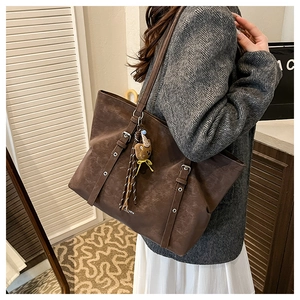 Detail of dark brown tote bag with decorative buckle strap and plush bear charm accent