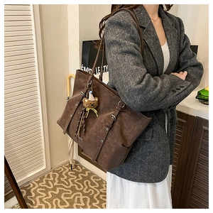 Detail of vintage brown tote bag with decorative buckles and cute plush bear charm
