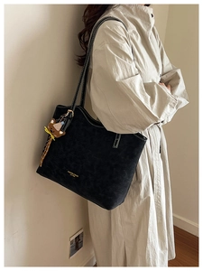 Detail of black faux leather tote with white stitching and bear charm on beige trench coat