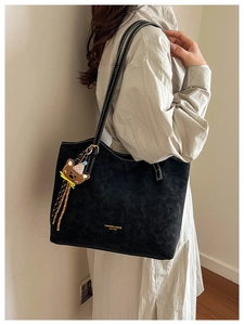 Detail of black suede tote bag featuring white contrast stitching and a cute bear charm