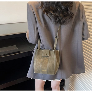 Detail of dark green bucket bag with white contrast stitching on grey blazer outfit