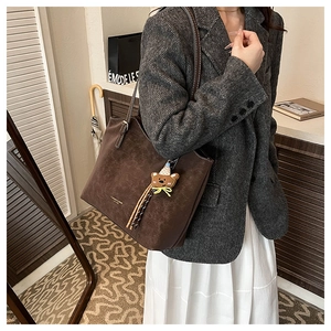 Detail of dark brown matte tote bag with shoulder straps and cute teddy bear charm pendant