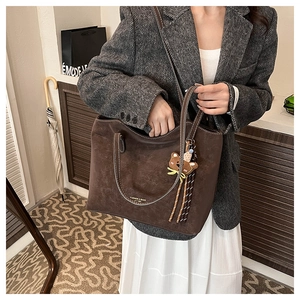 Detail of large brown matte tote bag with teddy bear pendant worn with a grey blazer