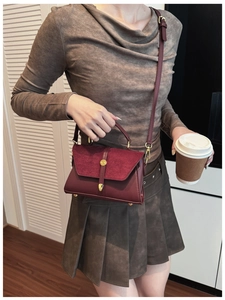 Dettaglio della borsa in pelle opaca bordeaux con chiusura dorata in scena lifestyle