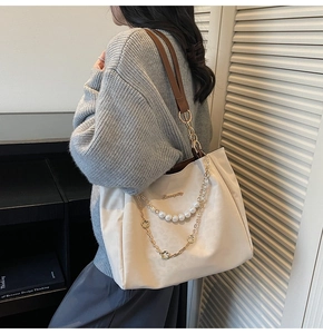 Detail of cream tote bag featuring elegant pearl and floral chain on brown leather strap