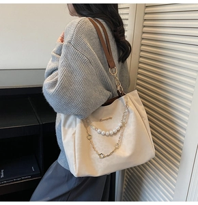 Close-up of large beige tote bag featuring pearl chain and metallic flower detail