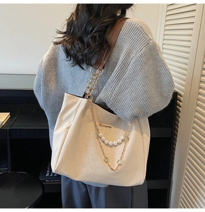 Dettaglio di una borsa tote bianco crema con grandi catene di perle e manici in pelle