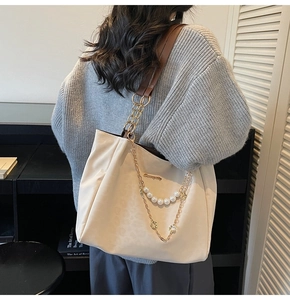Detail of cream leather tote bag featuring gold chains, pearl strings and metal logo