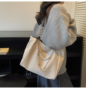Detail of cream tote bag featuring elegant gold chain with pearl and floral charms