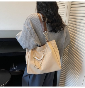 Detail of beige tote bag featuring pearl chain, gold floral strap, and metallic logo plate
