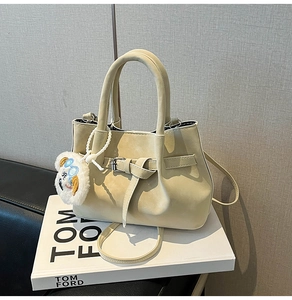 Detail of cream bucket bag with decorative buckle and plush charm on a book