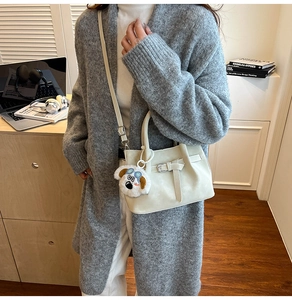 Détail d'un sac à main beige avec boucle métallique et pendentif chien en peluche